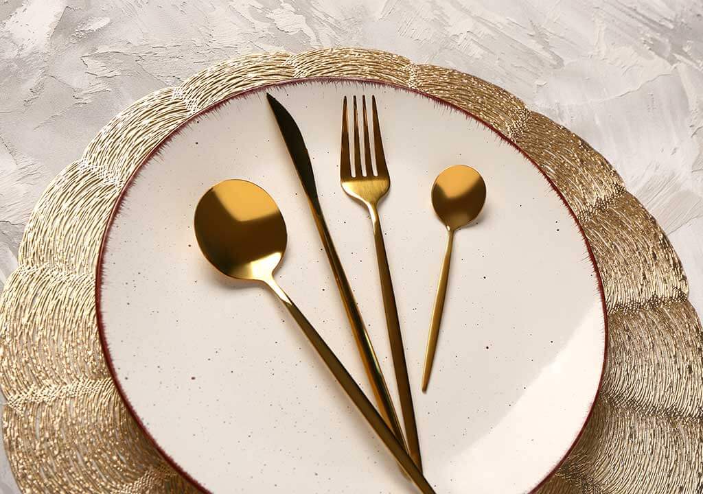 قاشق چنگال و کارد غذاخوری طلایی رنگ در بشقاب سفید رنگ